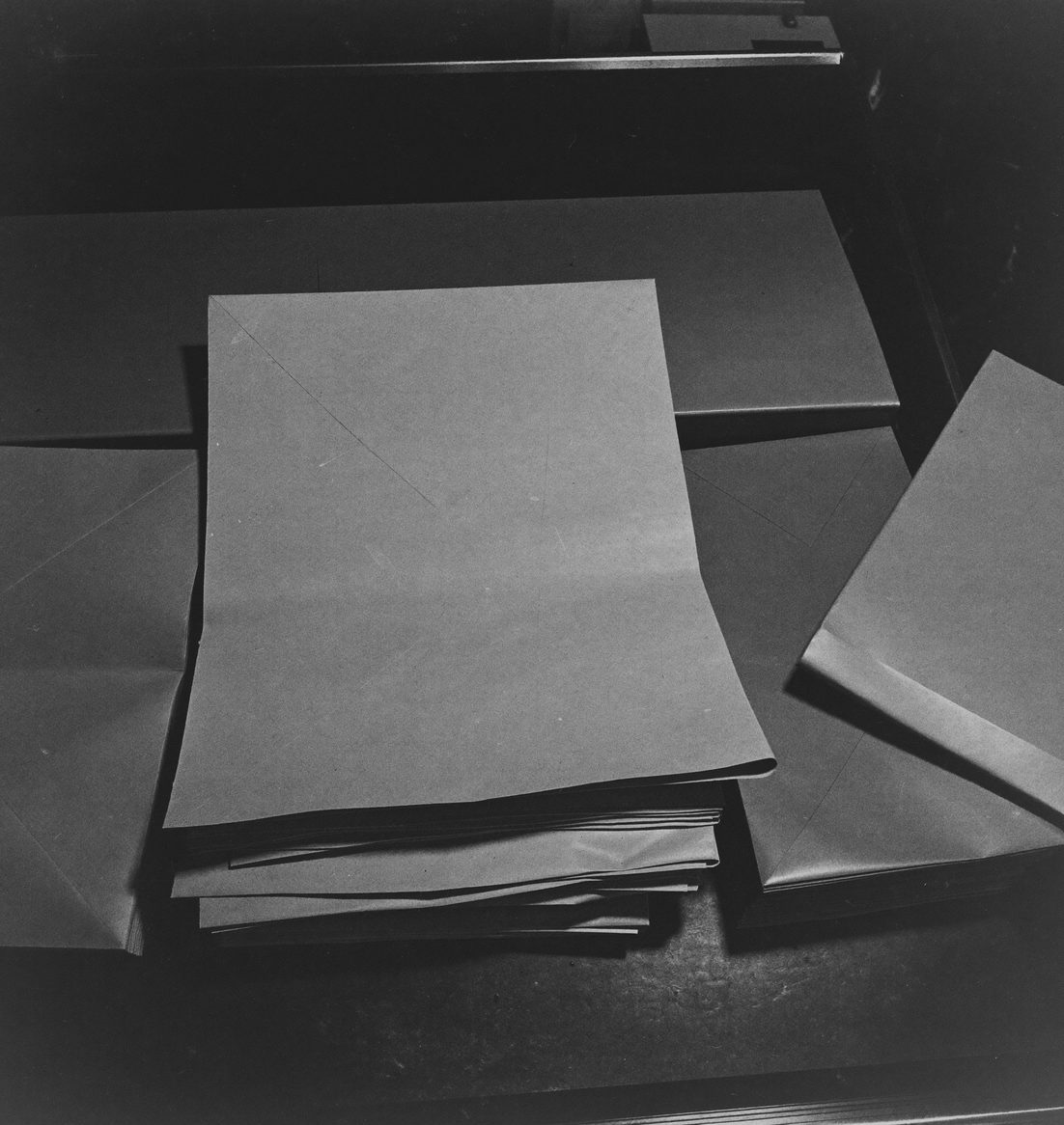Stacked flat unprinted folding cartons on a workbench, raking light on the fold creases