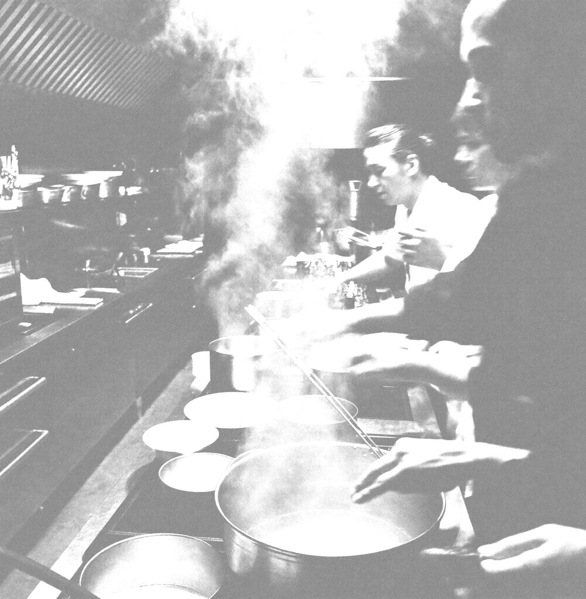 A busy professional kitchen pass in motion, steam rising, hands reaching, motion blur
