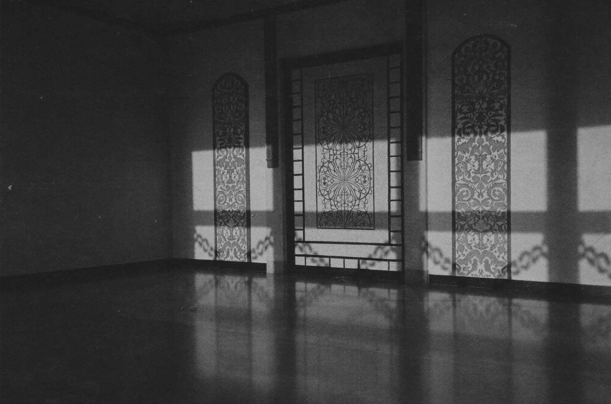 A hotel corridor with tall arched openings and hard sunlight patterns across the floor, no people