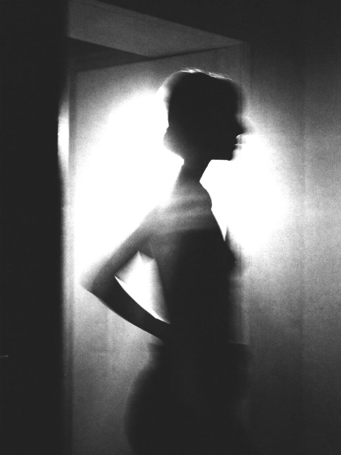 A motion-blurred figure walking past a bright doorway, extreme backlight, high contrast